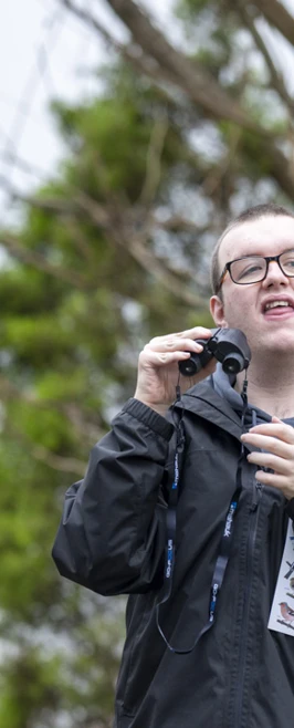 Young man holding binoculars and a bird identification chart while outdoors surrounded by trees. Young man holding binoculars and a bird identification chart while outdoors surrounded by trees.